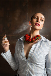 Miu Miu Miutine Eau de Parfum 100 ml being spritzed on model with strawberry necklace. Editorial Fashion Capaign image