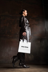 Model in Long leather trench coat walks with Miu Miu Bag in hand