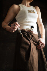 Miu Miu Miutine Eau de Parfum in 100ml and travel sized are tucked into the trouser waist band on a model wearing a Miu Miu Tank top. Editorial Fashion campaign image