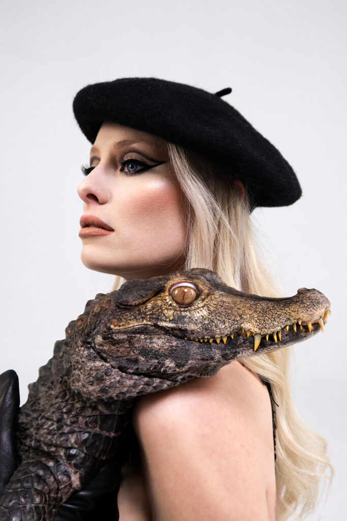 Utah editorial fashion portrait featuring a model in a black beret and opera gloves with a live caiman draped over her shoulder. Elevated branding photography with sculptural posing and graphic styling