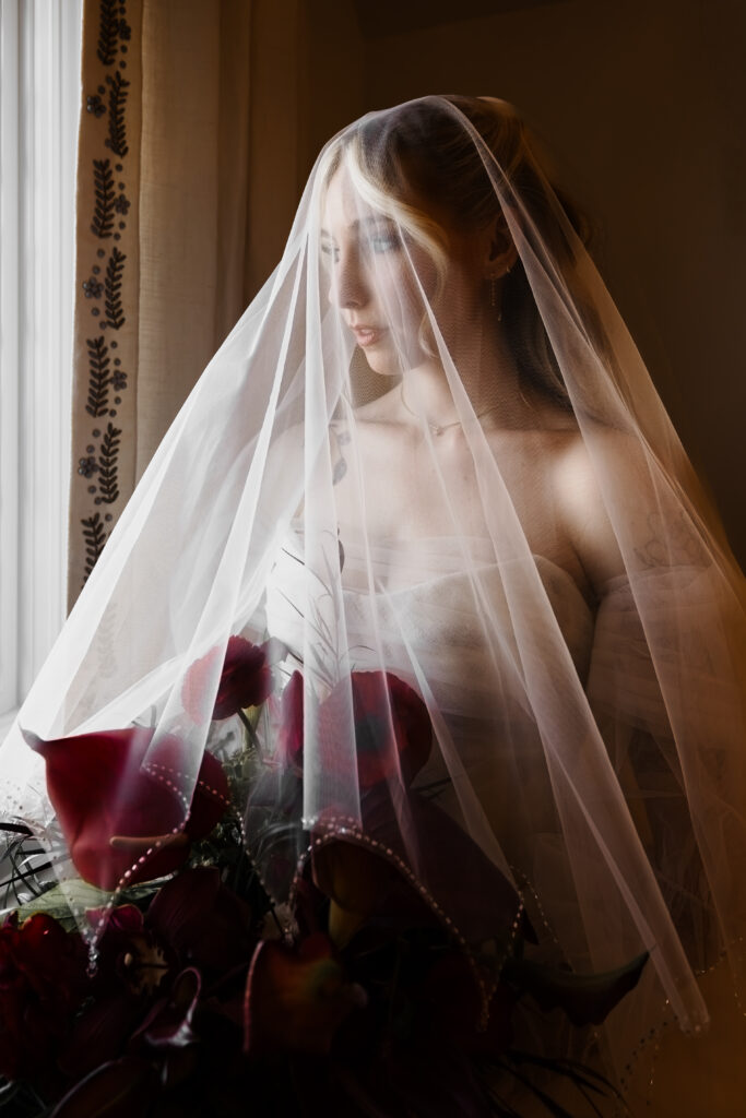 moody bridal portrait with veil over her face, red calla lily bouquet, at twenty and creek wedding venue in sandy utah